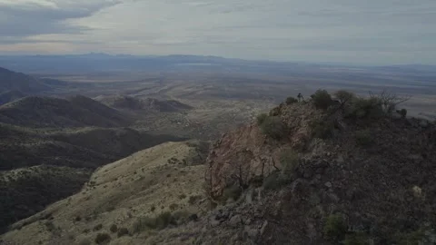 Aerial orbit of two men on top of a rugged desert mountain peak Stock Footage 328059088