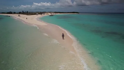 Aerial orbital view of a man walking and lying on the pristine white sandbar of Stock Footage 342586743