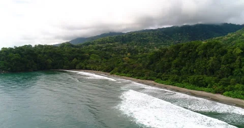 Aerial Over Ocean Surf, Waves And Beach With Lush Jungle Mountains And Clouds Stock Footage 135282811