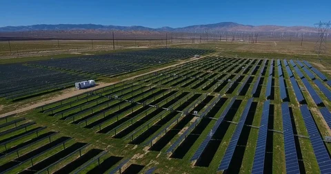 Aerial over solar panel field, with mountains and wind turbines in background Video stock 104813977