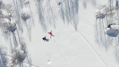 Aerial overhead view couple fall in snow enjoy making snow angels together .. Stockbeeldmateriaal 342276808