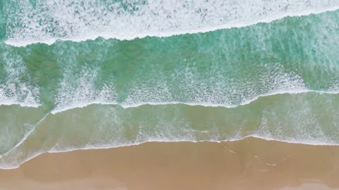 Aerial overhead view slow motion of ocean waves crashing onto sandy beach d.. Stockbeeldmateriaal 333940247