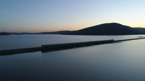 Aerial Pan Around of Train Passing on Tracks Over River at Sunset Stock Footage 94687887