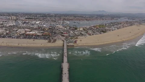 Aerial pan down over pier extending from beach city shore with waves breaking Stock Footage 157137997