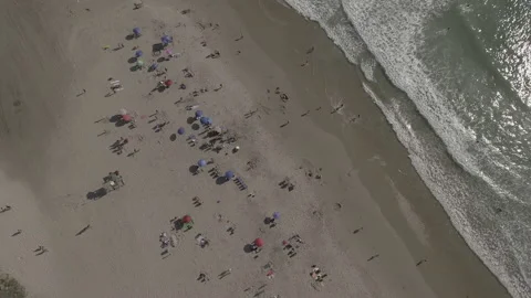 Aerial pan down over umbrellas on the beach with rolling waves Stock Footage 157132541