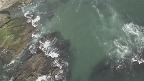 Aerial pan down over waves splashing on the rocks along the shore Stock Footage 157131988
