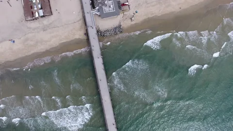 Aerial pan down over waves breaking along the pier on a sunny day Stock Footage 157137578