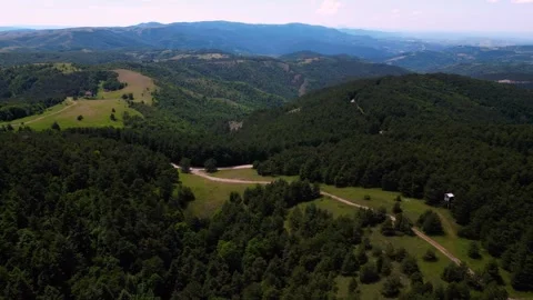 Aerial pan left over dirt road curving through green hills and forest Serbia Stock Footage 342241303