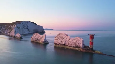 Aerial Pan of the Needles Lighthouse and Cliffs at Dawn with Golden Sky Stock Footage 338065696