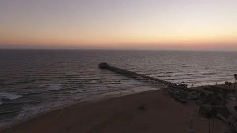 Aerial pan over the beach with waves rolling in at beach city pier at sunset Stock Footage 157119086