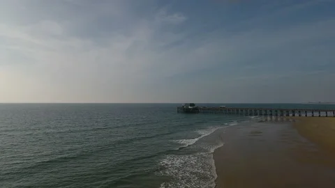 Aerial pan over rolling waves with a pier in the background on a sunny day Stock Footage 157177107