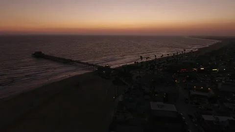 Aerial pan over waves continuously rolling into beach city pier at sunset Stock Footage 157119431