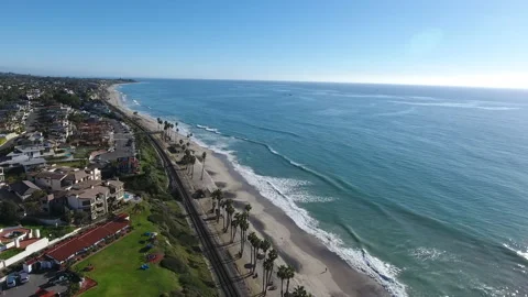 Aerial pan over waves rolling onto the shore by train tracks along the coast Stock Footage 157167872