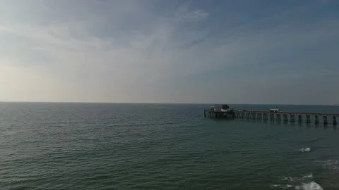 Aerial pan of a pier as waves roll in on a sunny day Stock Footage 157177129