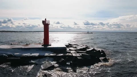 Aerial panning left: Waves hitting pier and lighthouse in winter with snow and Stock Footage 151882845
