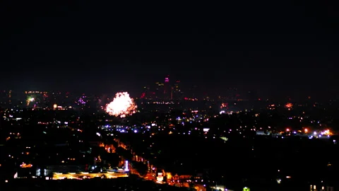 Aerial Panning Shot Of Fireworks Exploding Over Illuminated Cityscape, Drone Stock Footage 243878746