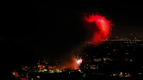 Aerial Panning Shot Of Fireworks Exploding On Suburb In City Against Sky, Drone Stock Footage 244020860