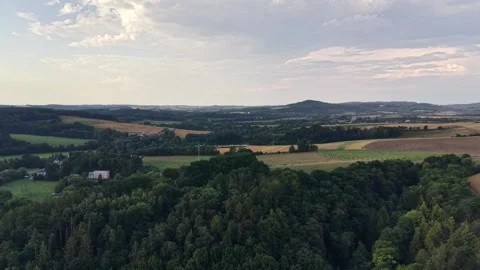 Aerial panorama over patchwork fields, forests, and distant hills under soft Stock Footage 348504248