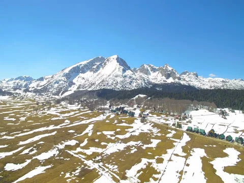 Aerial panorama of spring field and snow-capped mountain Stock Footage