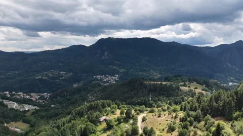 Aerial panoramic view over a lush green mountain valley and distant village unde 库存影片 341795494