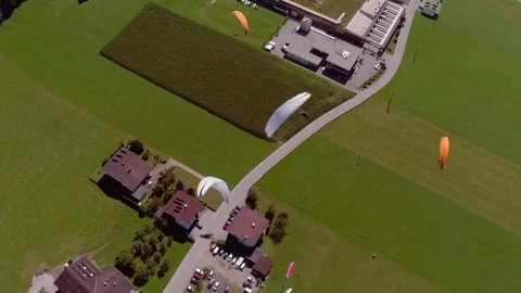 Aerial of paragliders gliding over the houses and green field Stock Footage