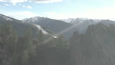 Aerial past cliffs and pine trees to reveal snowy Aspen ski resort in spring Vidéo 141627656