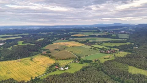 Aerial patchwork farmland over rolling hills with forest patches, winding roads, Stock Footage 342355480