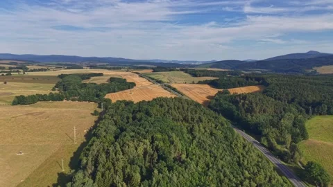 Aerial patchwork fields across rolling hills with winding road through rural Stock Footage 345170821