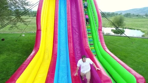 Aerial of people playing on a large inflatable slide during a family party Stock Footage 80271548