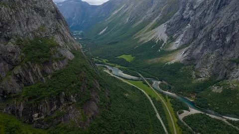 Aerial perspective of deep forested valley with turquoise river, winding road Stock Photos