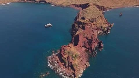 Aerial perspective of volcanic crimson cliffs bordering azure waters, luxury Stock Footage 308406336