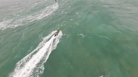 Aerial of pro surfer laying down on board in back of jet ski of another surfer Stock Footage 157704766