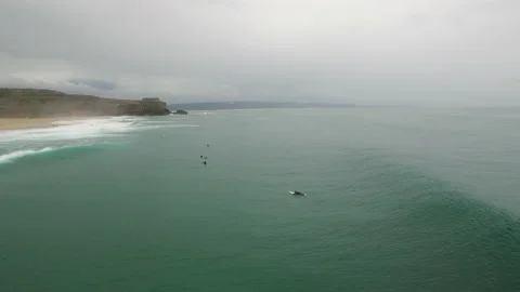 Aerial of pro surfer riding down ocean wave near other surfers on cloudy day Stock Footage 156002346