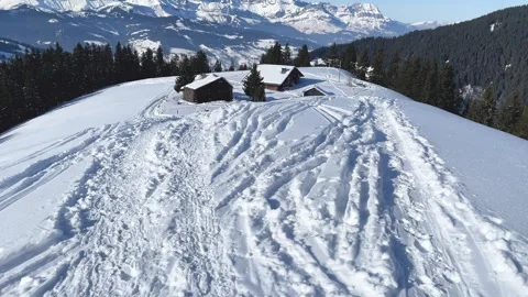 Aerial progression over snowy mountain terrain leading to alpine chalets at Stock Footage 346676246