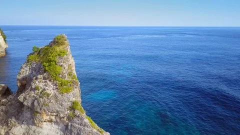 Aerial pull away shot of beach landscape with rocky cliff and wild blue sea Stock Footage 89359418