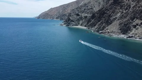 Aerial pull-away shot of a boat sailing in calm waters next to a mountain Video stock 333708573