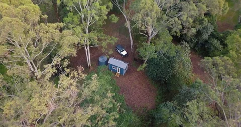 Aerial pull away from small blue cabin in the woods to reveal green tree tops Stock Footage 98270705