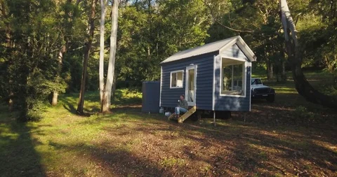 Aerial pull away through tree tops towards small cabin with female drinking t Stock Footage 98270707