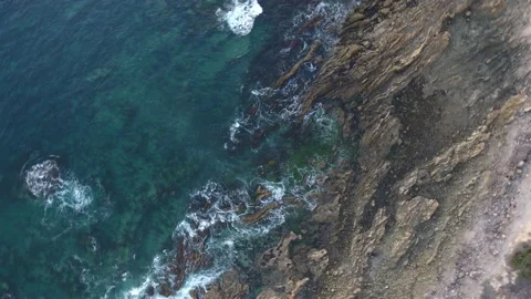 Aerial pull away of waves washing onto a rocky shore Stock Footage 157187904