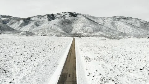 Aerial-Pull Back-Long straight snow lined road to mountain Stock Footage 99436134