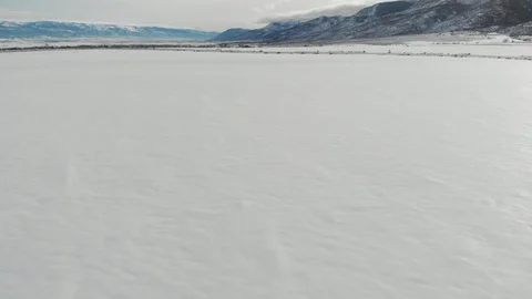 Aerial-Pull back low over unmarked snow field with shadowy mountain Stock Footage 101450600
