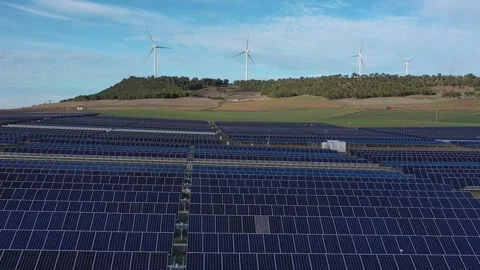 Aerial pull back over solar panels with wind turbines in background Stock Footage 327812296