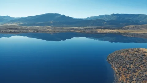 Aerial-Pull back over still blue lake with distant mountain reflection Video stock 112361097