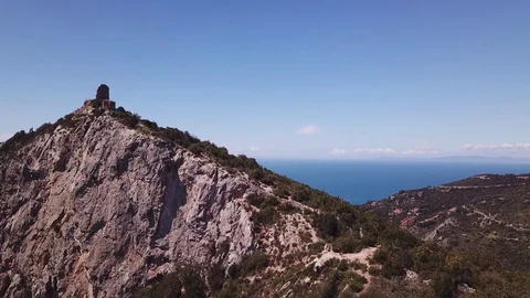 Aerial pull back from a peak with runs of a Tower on a cliff by the sea Stock Footage 107188949