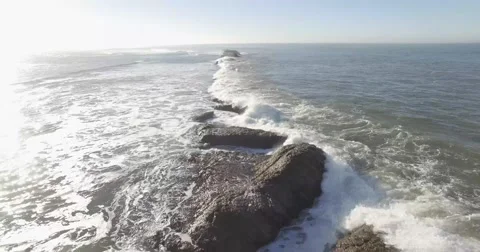 Aerial pull back shot over line of ocean rocks ending next to cliff in mornin Stock Footage 68212639