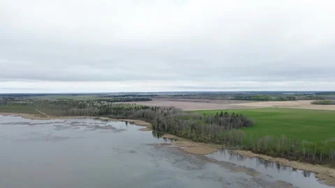 Aerial Pull-Back Shot from a Riverbank Over a Green Agricultural Field Stock Footage 312417679