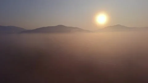 Aerial pull back through thick morning mist and golden sunrise sun Stock Footage 334359310