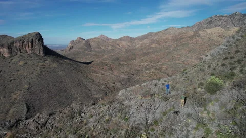 Aerial pullback of 2 men hiking on a rugged mountain ridge in the desert Stock Footage 231781182