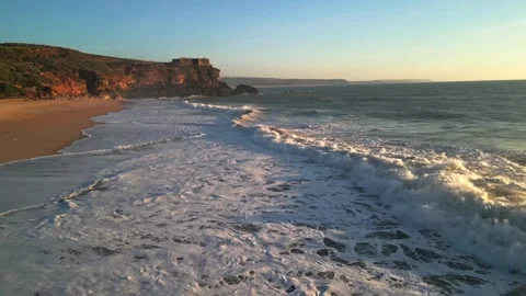 Aerial pullback over ocean waves and cliffside beach at golden hour Stock-Footage 333498850