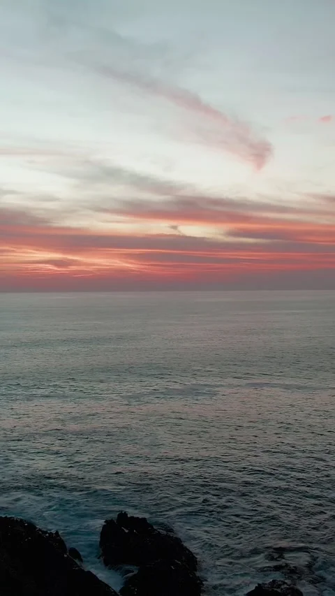 Aerial pullback reveals rocky coast beneath colorful sunset skies at Faro de Stock-Footage 336466502